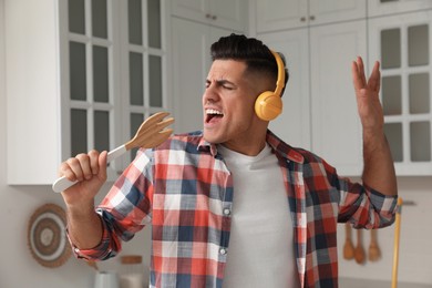 Man with headphones and fork spatula singing in kitchen