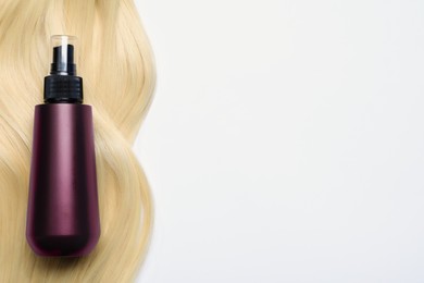 Photo of Spray bottle with thermal protection and lock of blonde hair on white background, flat lay. Space for text