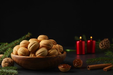 Photo of Homemade walnut shaped cookies with boiled condensed milk, cinnamon sticks, candles and fir branches on black table, space for text