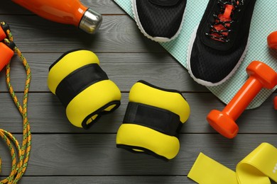 Yellow weighting agents and sport equipment on grey wooden table, flat lay