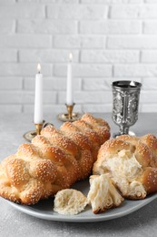 Homemade braided bread with sesame seeds, goblet and candles on grey table, closeup. Traditional Shabbat challah