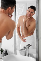 Handsome man touching his smooth face after shaving near mirror in bathroom