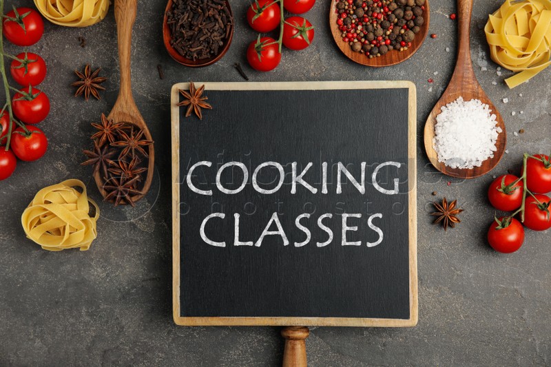 Small chalkboard with inscription Cooking Classes and different fresh products on grey table, flat lay