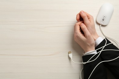 Man showing hands tied with computer mouse cable at white wooden table, top view. Internet addiction
