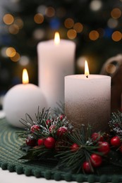 Beautiful burning candles and Christmas decor on white table against festive lights