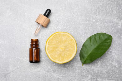 Bottle of essential oil with lemon slice and leaf on grey table, flat lay