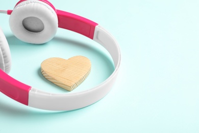 Modern headphones and wooden heart on turquoise background, space for text. Listening love music songs