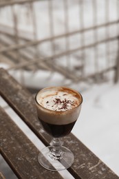 Glass of aromatic coffee with chocolate powder on wooden bench outdoors in winter