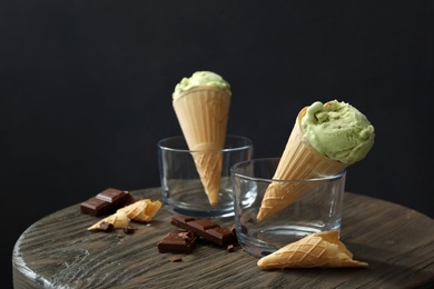 Delicious pistachio ice cream in wafer cones and chocolate pieces on wooden table. Space for text