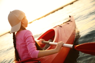 Little girl kayaking on river at sunset. Summer camp activity