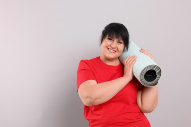 Happy overweight mature woman with yoga mat on grey background, space for text