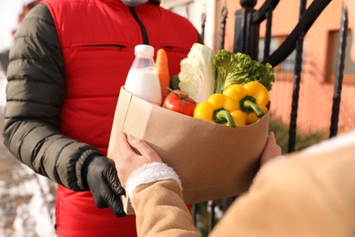 Courier giving paper bag with groceries to woman outdoors, closeup. Delivery service during Covid-19 quarantine