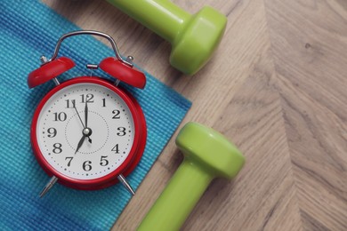 Alarm clock, yoga mat and dumbbells on wooden background, flat lay. Morning exercise