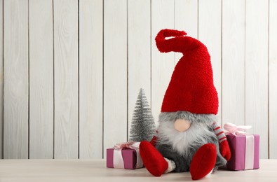 Cute Christmas gnome, gift boxes and small decorative fir tree on table against white wooden background. Space for text