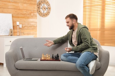 Young man playing chess with partner through online video chat in living room