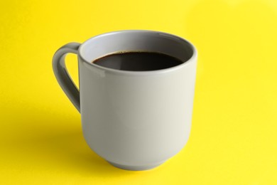 Grey mug of freshly brewed hot coffee on yellow background