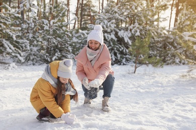Mother and daughter rolling snowballs in winter forest