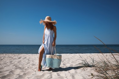 Woman with beach bag and straw hat on sand near sea