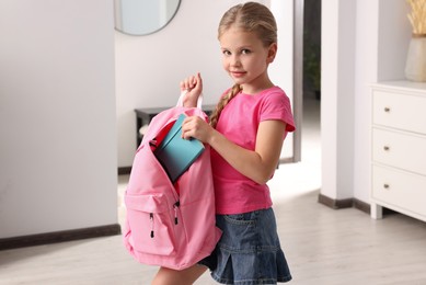 Little girl putting notebook in pink backpack at home. Preparing to school