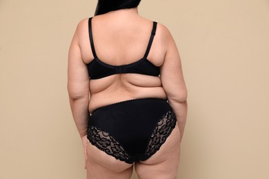 Back view of overweight woman in black underwear on beige background. Plus-size model