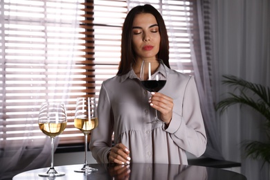 Beautiful young woman tasting luxury wine at table indoors