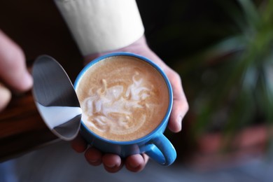 Barista pouring milk into cup of coffee on blurred background, closeup. Space for text