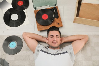 Man listening to music with turntable while lying on floor at home, above view