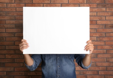 Man holding white blank poster near red brick wall. Mockup for design
