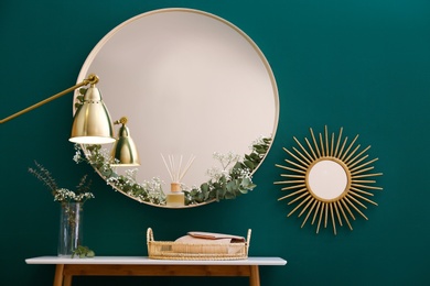 Round mirror and table with accessories near green wall in modern room interior