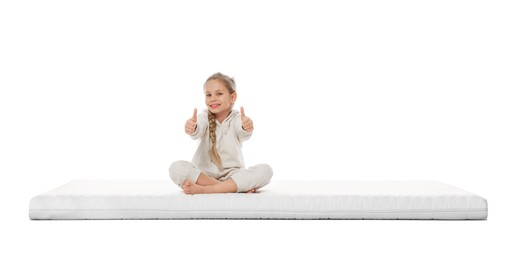 Little girl sitting on mattress and showing thumbs up against white background