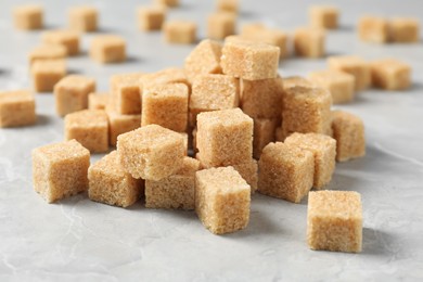 Photo of Heap of brown sugar cubes on light grey marble table, closeup