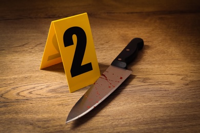 Bloody knife and crime scene marker on wooden table