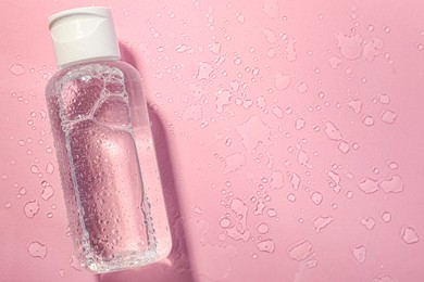 Wet bottle of micellar water on pink background, top view. Space for text