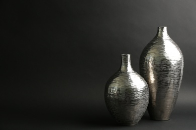 Stylish silver ceramic vases on black background, space for text