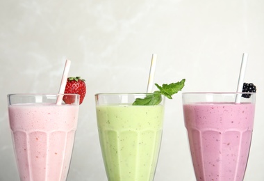 Tasty milk shakes with fresh berries and mint on light background, closeup