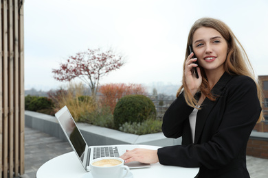 Photo of Businesswoman with laptop talking on phone in outdoor cafe. Corporate blog