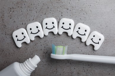 Plastic teeth with cute faces, toothpaste and brush on grey background, flat lay