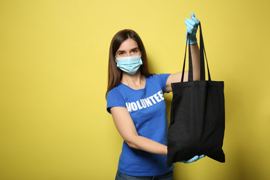 Female volunteer in protective mask and gloves with black bag on yellow background, space for text. Aid during coronavirus quarantine