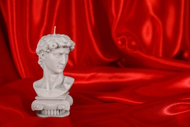 Beautiful David bust candle on red satin. Space for text