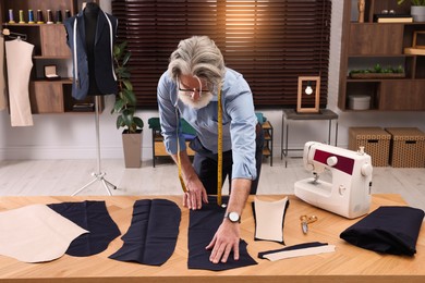 Professional tailor working with fabric at table in atelier