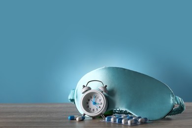 Sleeping mask, alarm clock and pills on wooden table. Insomnia treatment