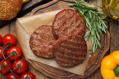 Tasty grilled hamburger patties, vegetables and rosemary on wooden table, flat lay