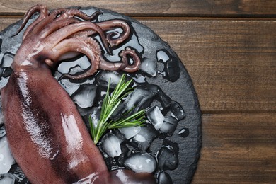 Photo of Fresh raw squid with ice and rosemary on wooden table, top view