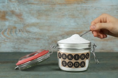 Woman taking baking soda with spoon from jar at light blue wooden table, closeup