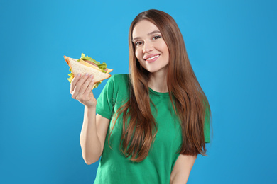 Photo of Young woman with tasty sandwich on light blue background