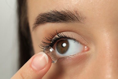 Woman putting contact lens in her eye on blurred background, closeup