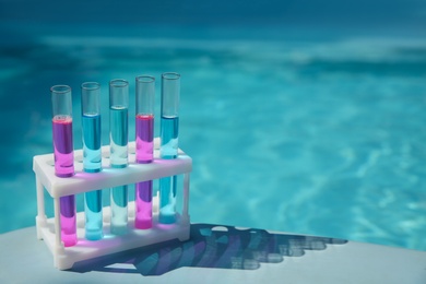Test tubes with reagents in rack near swimming pool. Space for text