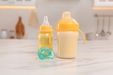 Baby bottles and pacifier on white marble table indoors. Maternity leave concept