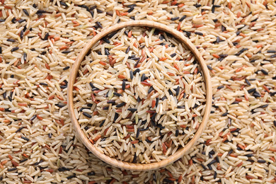 Mix of different brown rice and wooden bowl, top view