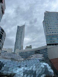 Photo of WARSAW, POLAND - JULY 17, 2022: Big shopping mall and buildings under cloudy sky, low angle view